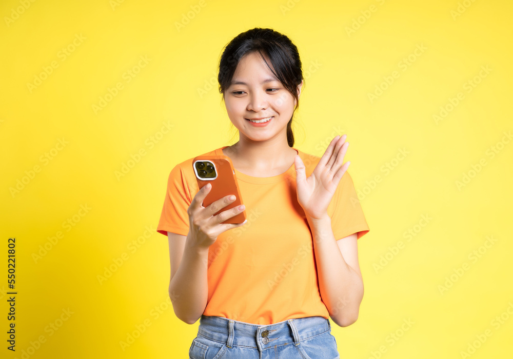 image of asian girl holding phone and isolated on yellow background image of asian girl holding phone and isolated on yellow background
