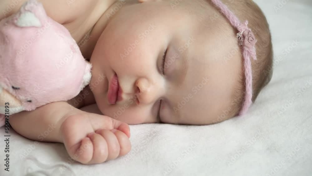 Close up of little newborn baby girl sleeps with soft pink toy. Love and child care Close up of little newborn baby girl sleeps with soft pink toy. Love and child care