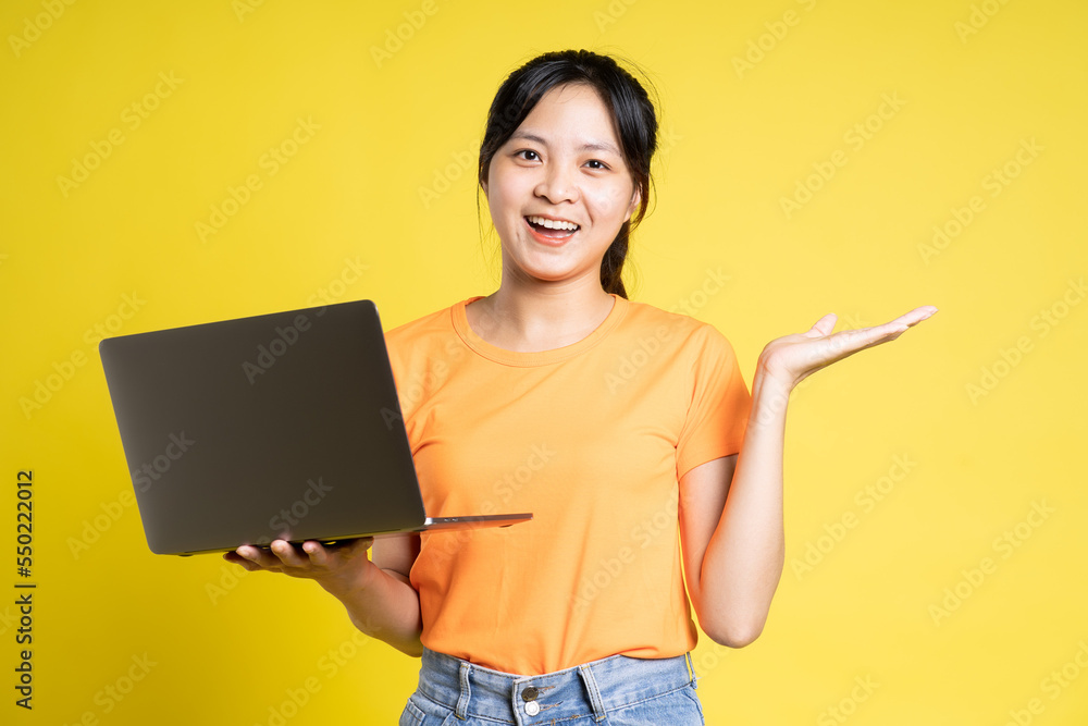 image of asian girl holding laptop and isolated on yellow background image of asian girl holding laptop and isolated on yellow background