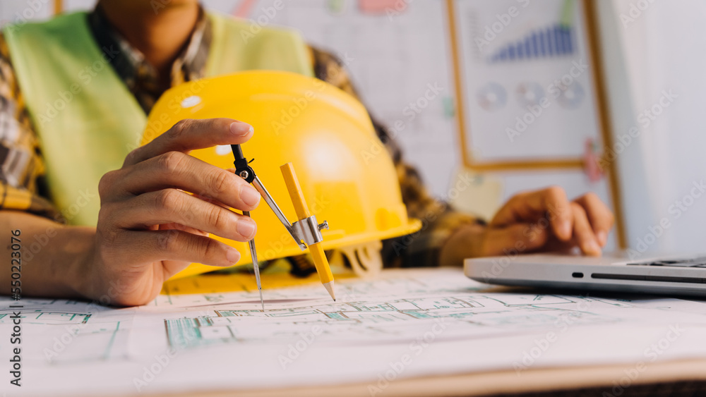 Two colleagues discussing data working and tablet, laptop with on on architectural project at construction site at desk in office Two colleagues discussing data working and tablet, laptop with on on architectural project at construction site at desk in office