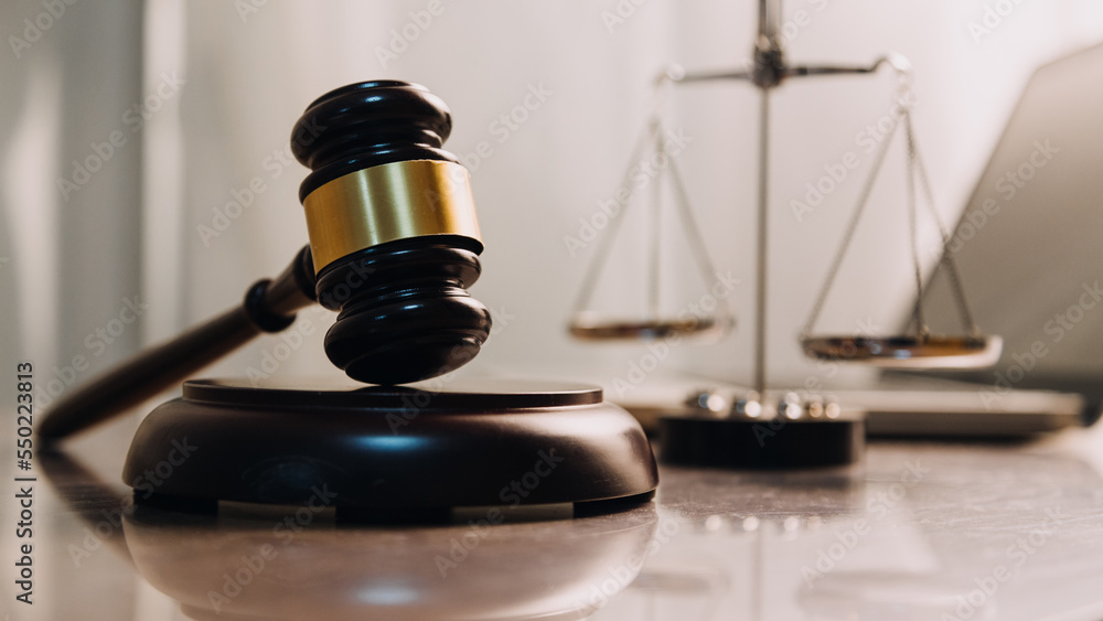 Justice and law concept.Male judge in a courtroom with the gavel, working with, computer and docking keyboard, eyeglasses, on table in morning light Justice and law concept.Male judge in a courtroom with the gavel, working with, computer and docking keyboard, eyeglasses, on table in morning light