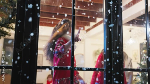 Adorable child look through the window and admiring first snow flakes. photo