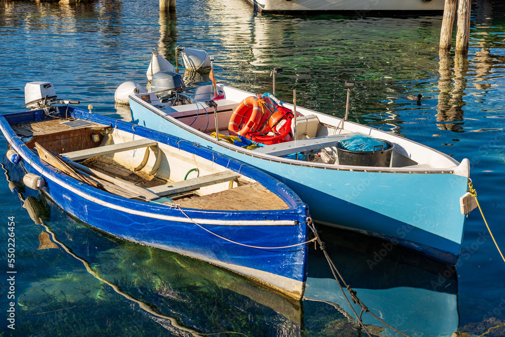 Closeup of two small wooden fishing boats moored in the small port of the Malcesine village, tourist resort on the coast of lake Garda. Verona province, Veneto, Italy, southern Europe. Closeup of two small wooden fishing boats moored in the small port of the Malcesine village, tourist resort on the coast of lake Garda. Verona province, Veneto, Italy, southern Europe.