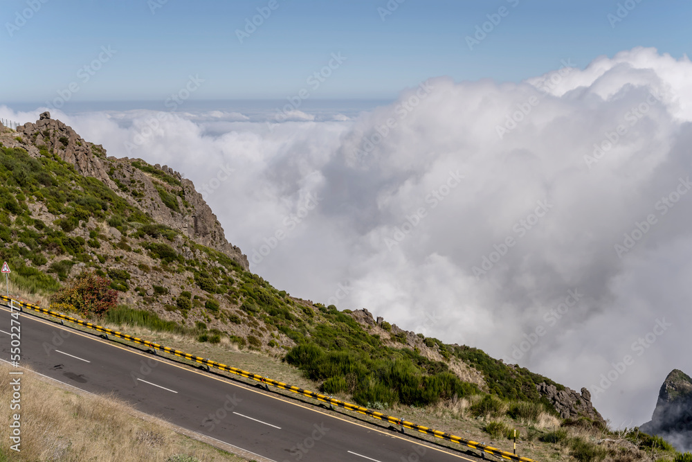 Fototapeta premium panoramic road with barrier on slope above the clouds at Miradouro de Areeiro peak, Madeira