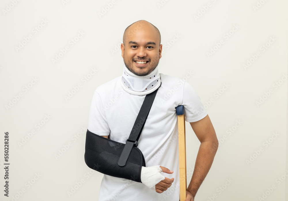 © Chanakon - Happy young asian man broken arm and leg on isolated. Man put on plaster cast splint with walking sticks crutches. Patient wearing sling support arm with neck collar. life insurance and accident