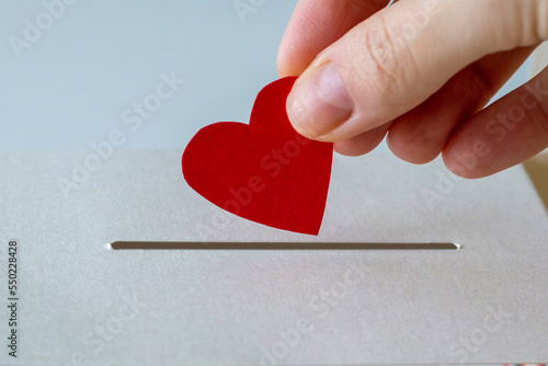 The concept of donations. A woman's hand places her heart in a slit of a box in close-up.