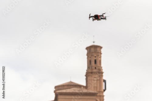 Video recording quadcopter drone flying in a clear sky near a church