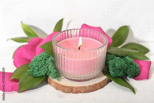 pink soy wax candle burning on a wooden saw cut podium with floral decor. Valentines day decoration for a holiday table set.