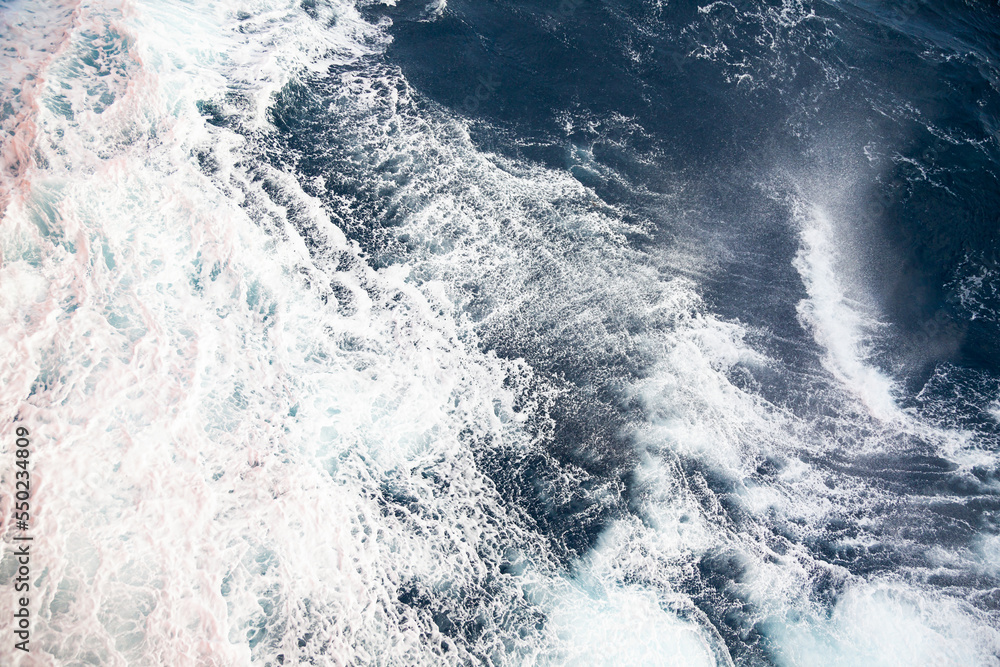 Fototapeta premium Rushing water in the open sea. Blue water background with white foam.