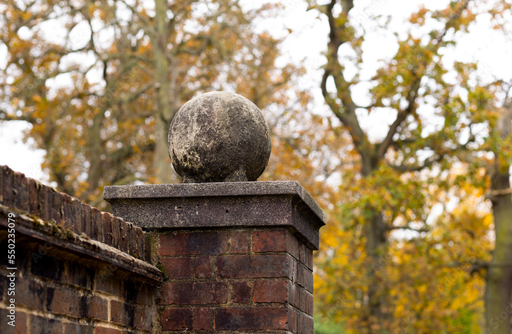 Stone ball on the wall pedestal against the background of autumn trees. Stone ball on the wall pedestal against the background of autumn trees.