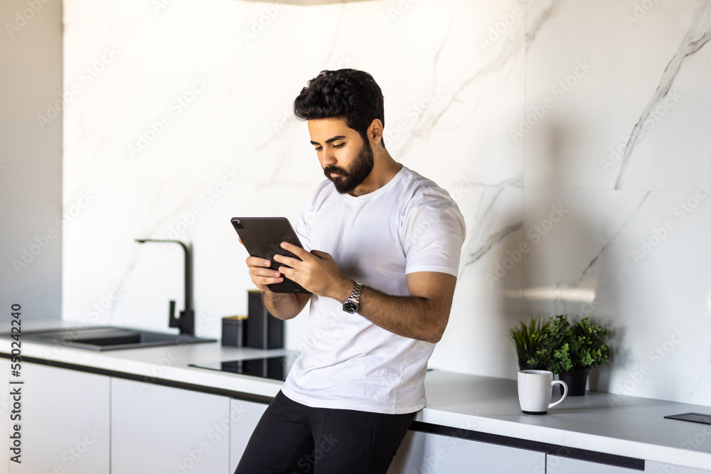 Confident man using tablet preparing vegetable salad in kitchen. Young chef searching recipes, ordering food online, watching cooking videos preparing healthy food at home.