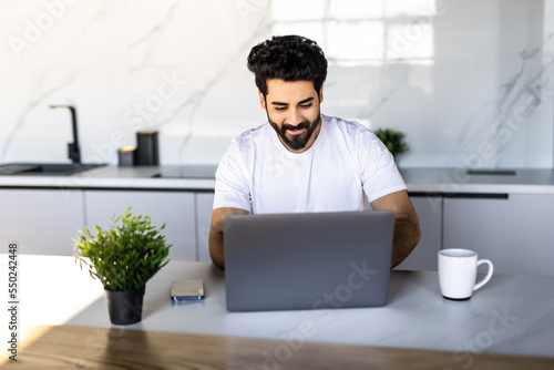 Pensive indian man freelancer having snack while working from home during coronavirus pandemic, stressed arab guy eating healthy food, looking at laptop screen.