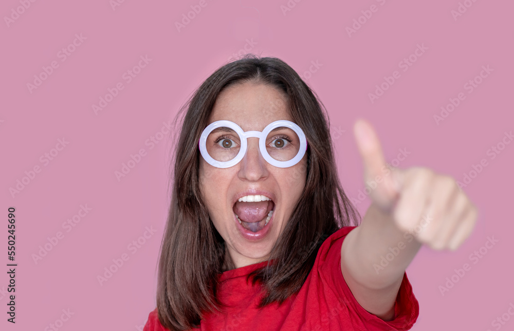woman red t shirt wow face holding in front finger thumbs up isolated on pink.advertising banner copy paste christmas march 8th women mothers day celebration.female wear wizard round frame glasses woman red t shirt wow face holding in front finger thumbs up isolated on pink.advertising banner copy paste christmas march 8th women mothers day celebration.female wear wizard round frame glasses