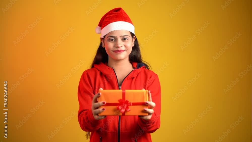 Beautiful young woman with Christmas gift box, Asian Indian girl wearing Santa cap isolated over colour studio background Beautiful young woman with Christmas gift box, Asian Indian girl wearing Santa cap isolated over colour studio background