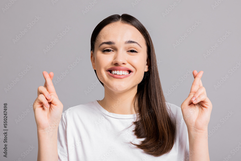 Dreamy young woman in white casual t-shirt isolated on grey background crossing fingers smiling at camera. Dreamy young woman in white casual t-shirt isolated on grey background crossing fingers smiling at camera.