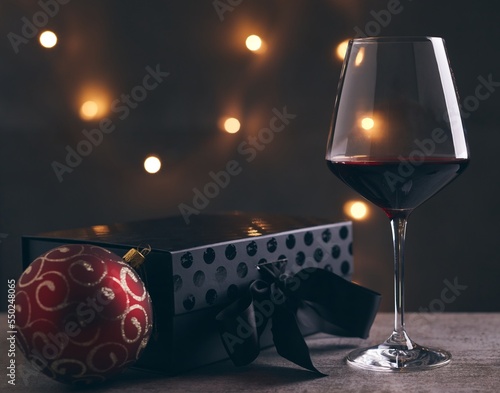 Glass of red wine with black gift box and Christmas decorations on table. Christmas lights in the black background.