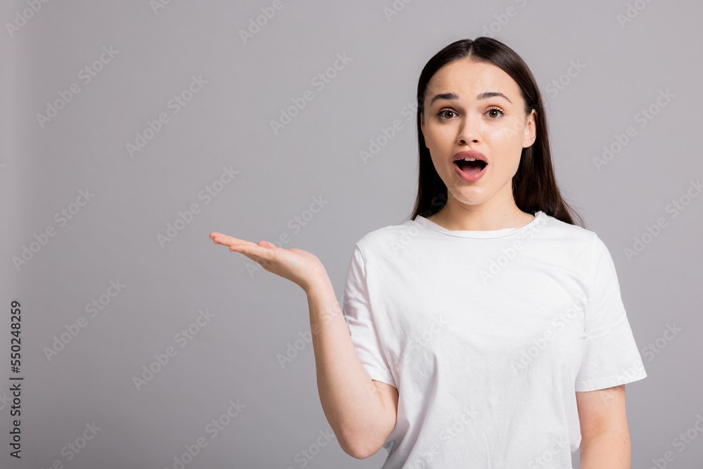 Surprised woman standing on grey background in studio isolated copyspace holding open hand presenting something blanket. Surprised woman standing on grey background in studio isolated copyspace holding open hand presenting something blanket.