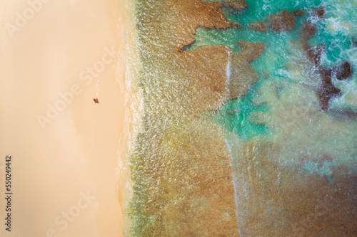 Drone View of a man having a beautiful beach walk next to a coral reef. Thailand