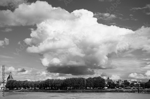 Black and white photograph of a bubble shaped cloud hanging above a tree line and a city