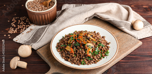 Plate with tasty cooked lentils and mushrooms on wooden table