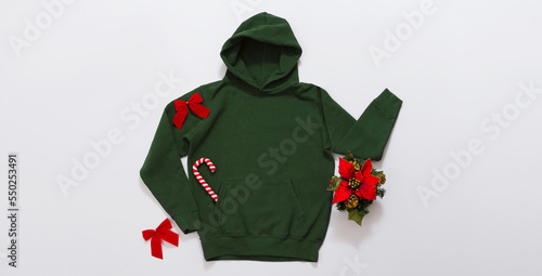 Close up banner green blank template hoodie copy space. Christmas Holiday concept. Top view mockup hoodie. Red holidays decorations on jumper white background. Happy New Year accessories. Xmas