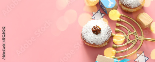 Menorah, dreidels and donuts for Hanukkah celebration on pink background with space for text