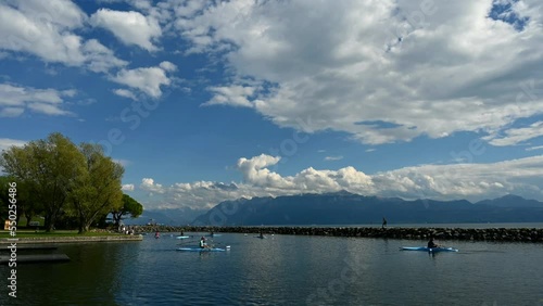 Rowing team on water. Landscape of Lake Geneva, tree, sky and clouds. Time lapse. Lausanne, Vaud Canton, Switzerland.