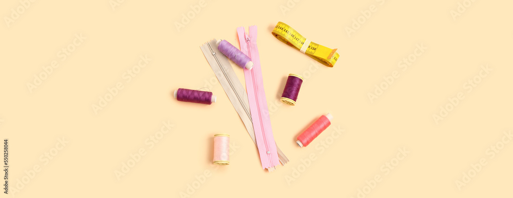 Thread spools, measuring tape and zippers on beige background Thread spools, measuring tape and zippers on beige background