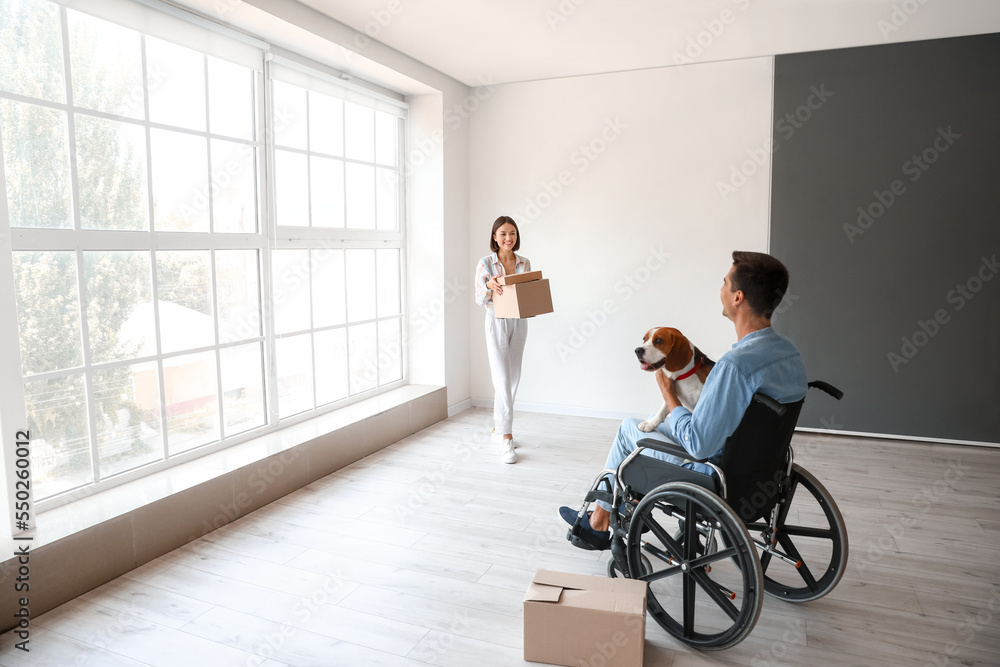 Young woman and her husband in wheelchair with dog in their new flat on moving day Young woman and her husband in wheelchair with dog in their new flat on moving day