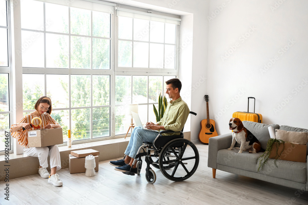 Young woman with her husband in wheelchair and dog packing things in room on moving day Young woman with her husband in wheelchair and dog packing things in room on moving day