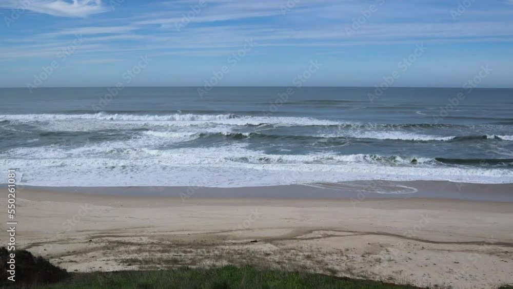 Waves crashing on to sandy beach with blue skies and horizon line visible, Atlantic Ocean, Portugal Waves crashing on to sandy beach with blue skies and horizon line visible, Atlantic Ocean, Portugal