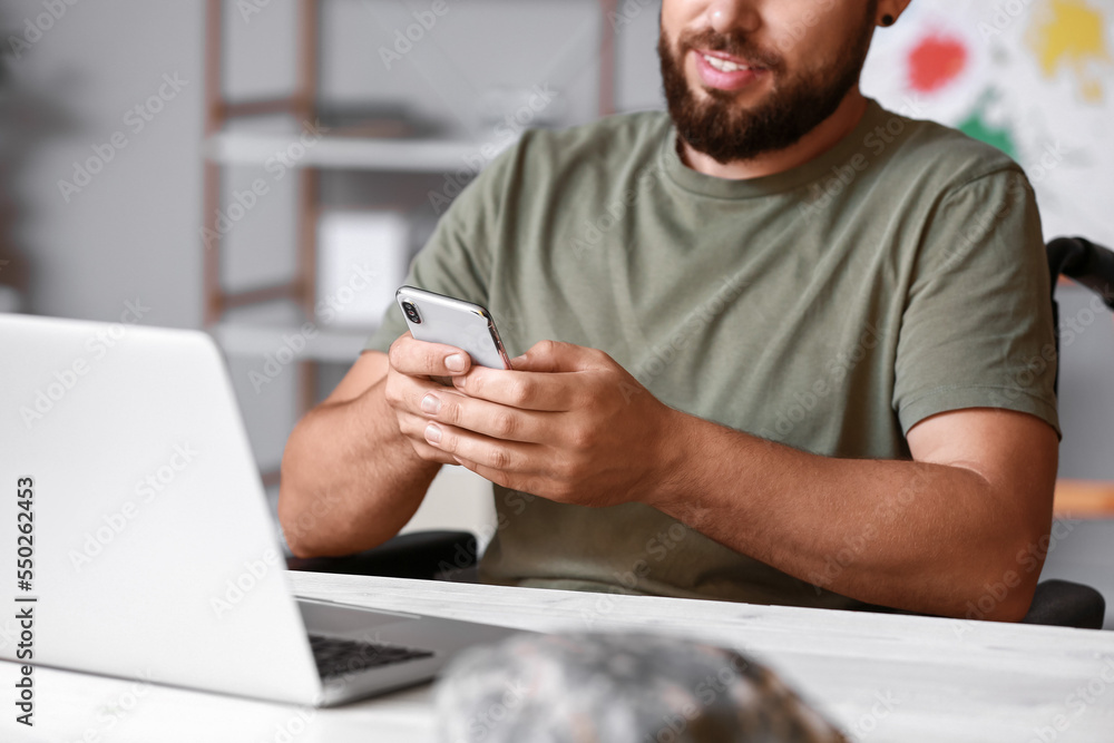 Soldier in wheelchair using mobile phone at home, closeup Soldier in wheelchair using mobile phone at home, closeup