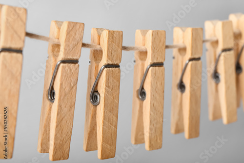 Wooden clothespins hanging on rope against grey background, closeup