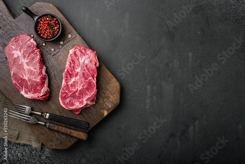 Raw top blade cut organic meat with rosemary, on black dark stone table background, top view flat lay, with copy space for text