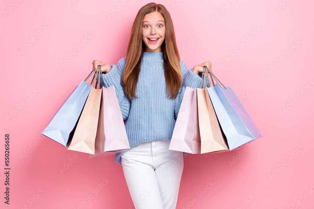 Photo of young funny overjoyed schoolkid girl wear blue knitted sweater hold stack packages from shopping sale isolated on pink color background