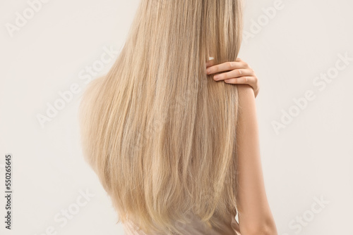 Woman touching blonde hair on light background