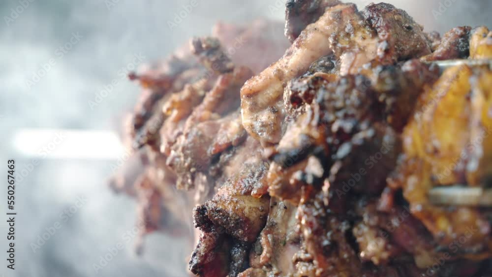 Homemade marinated and seasoned meat tenderloin slowly rotating on steel spit on burning fire, meat pieces with crispy crust roasting in barbecue smoker for picnic party. Meat cookout, roasting