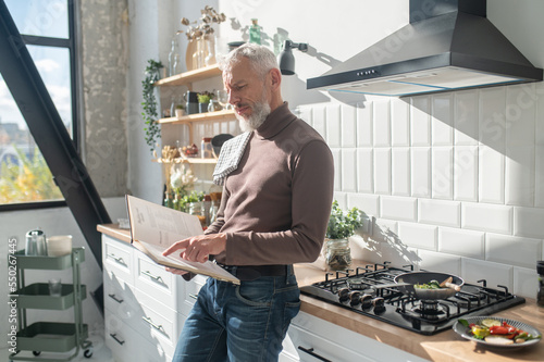 Bearded mature man seasrching for a recepy in a cookery book photo