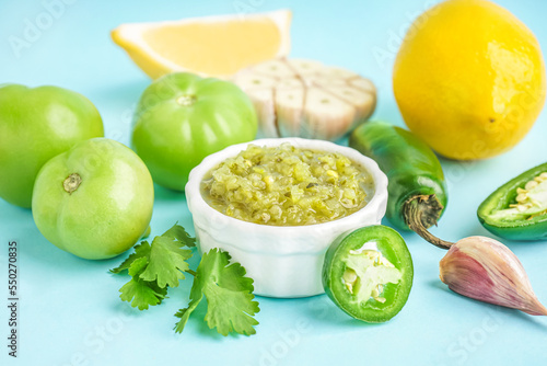 Bowl of tasty green salsa sauce with ingredients on color background