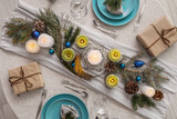 Christmas table setting with fir branches, candles and gifts in dining room, top view