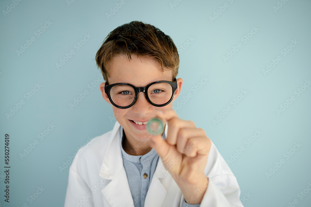 young cool boy ,with big massive black glasses is dressed up as a mad scientist holding beaker and vials in hand in front of blue background young cool boy ,with big massive black glasses is dressed up as a mad scientist holding beaker and vials in hand in front of blue background