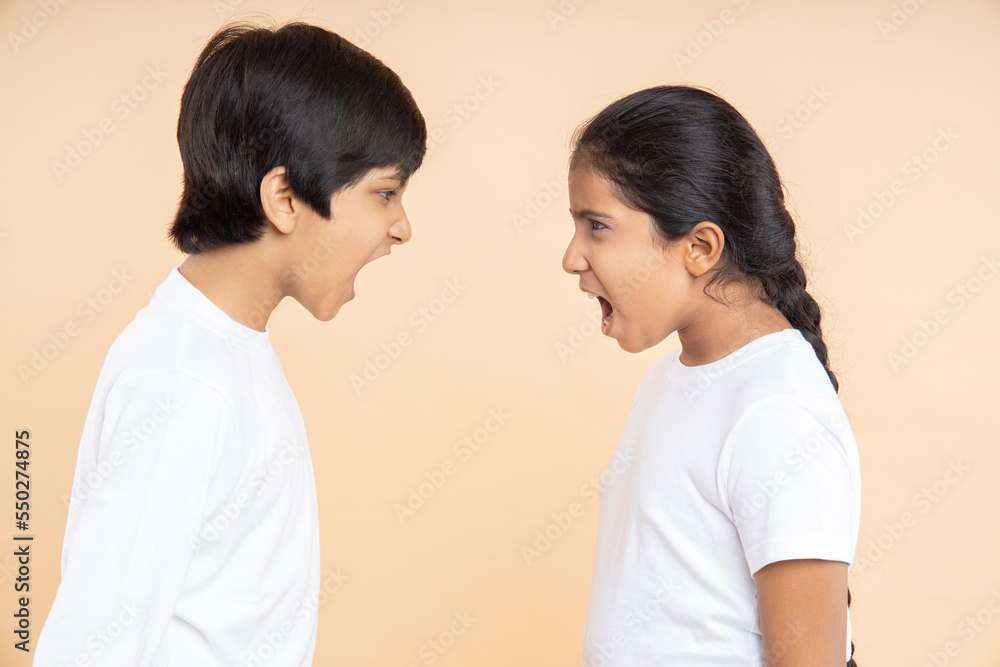 Angry little indian kids shouting and fighting with each other isolated over beige studio background, Frustrated boy and girl screaming. Angry little indian kids shouting and fighting with each other isolated over beige studio background, Frustrated boy and girl screaming.