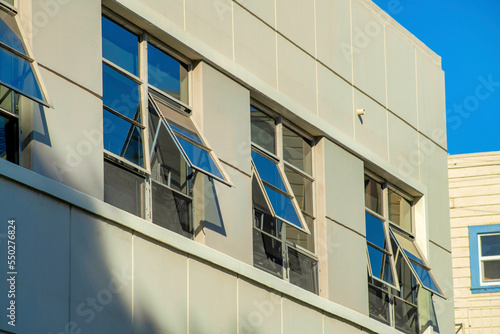 Beige stucco building with visible school wedge windows with tinting and clear blue sky background in late afternoon sun downtown