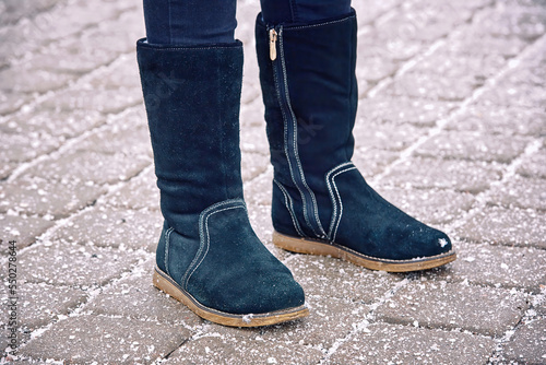 Winter boots on road with rock salt, chemical reagents to melt ice, prevent icing. Salt can ruin footwear in winter season. Salt sprinkled on pavement, prevent sliding, deicing mixture on paving stone