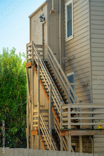 Two sets of brown wooden stairs or steps on exterior of wooden or timber house in shade with back yard trees and blues sky © Aaron