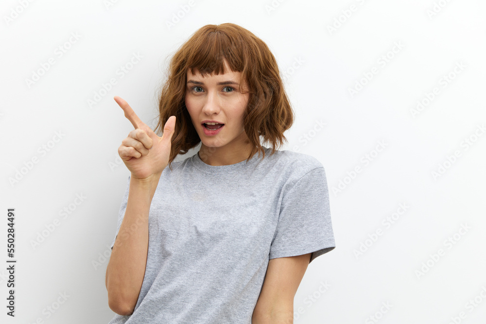 a happy, joyful woman with red hair color and beautiful styling looks smiling, pointing her finger at an empty space. a happy, joyful woman with red hair color and beautiful styling looks smiling, pointing her finger at an empty space.