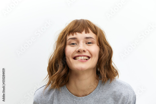 a happy, joyful woman in a gray cotton T-shirt stands against a light background, smiling happily and looking at the camera. Horizontal photo with an empty space for inserting an advertising layout © Tatiana