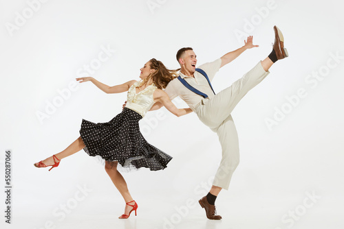 Fototapeta Naklejka Na Ścianę i Meble -  Young excited man and woman in 60s american fashion style clothes dancing retro dance isolated on white background. Music, energy, happiness, mood, action