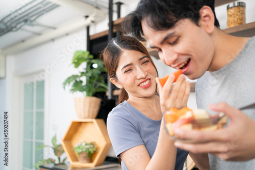 Healthy young Asian couple feeding a fresh sliced tomato together with a smile and happy emotion. An active lifestyle with healthy and vegetarian food advertisement. Image with copy space.