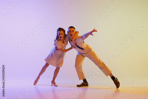 Fototapeta Naklejka Na Ścianę i Meble -  Incendiary dance. Emotional couple of dancers in retro style outfits dancing social dances isolated on gradient lilac color background in neon light. Concept of art, 60s, 70s culture